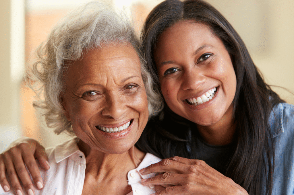 A home care worker poses with an elderly woman smiling looking at the camera.